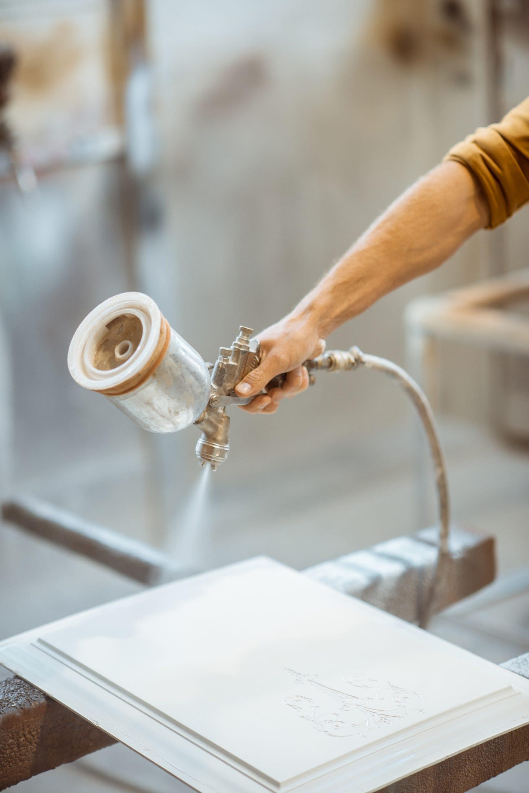 Painting wooden product with a spray gun at the painting shop of the carpentry, close-up
